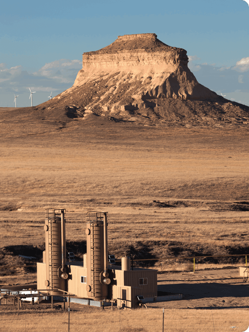 An industrial plant with a desert mesa backdrop under a blue sky.