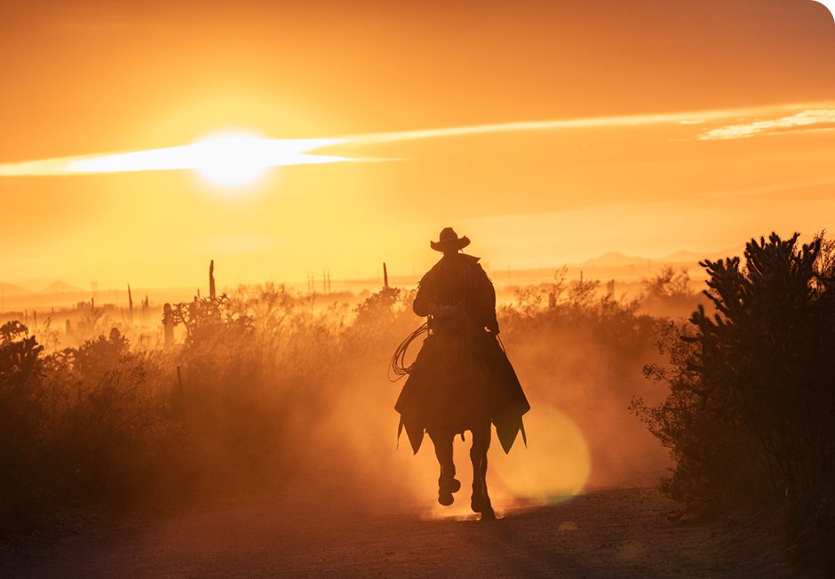A cowboy rides into the sunset on horseback through dusty terrain.
