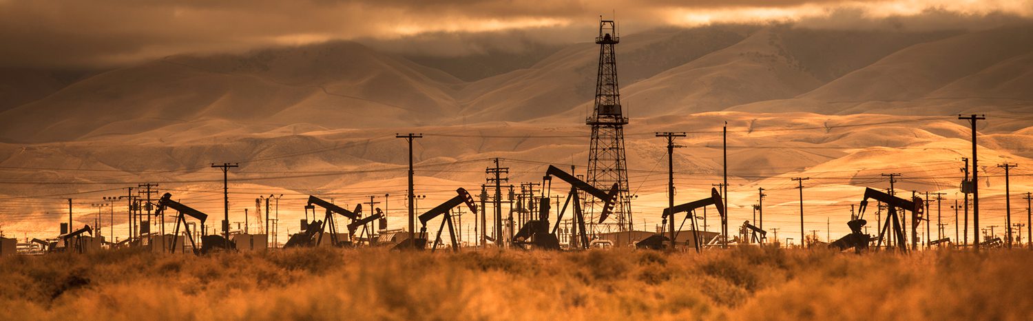 Oil pumps and drilling rigs silhouetted against a dramatic sunset sky.