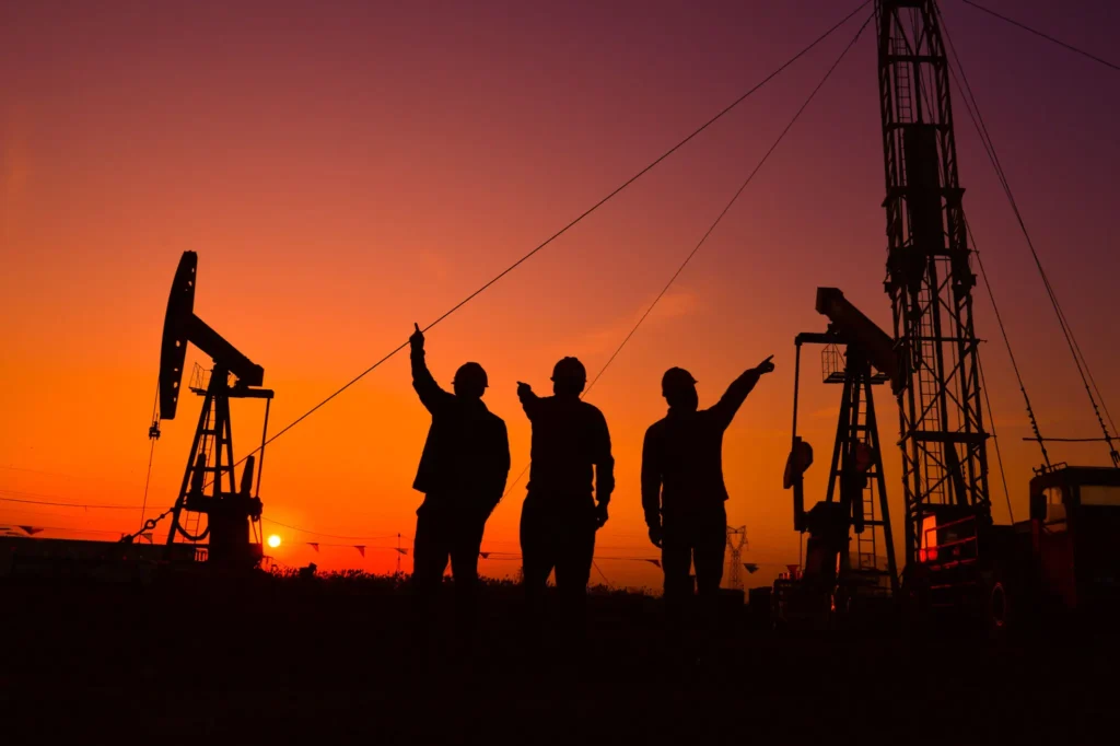Silhouettes of three workers at an oil rig during sunset.