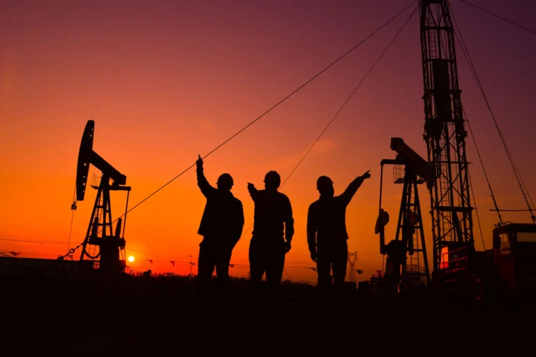 Silhouettes of three workers at an oil rig during sunset.
